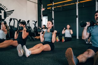 Demo post photo: a District H class pressing dumbbells together on the gym floor