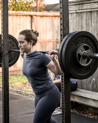 Demo post photo: a member back squatting on the District H outdoor rig at golden hour